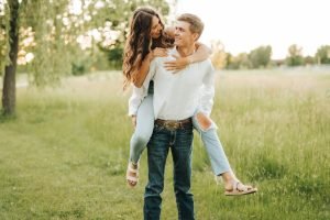 Engaged couple piggy back ride in grass field