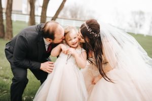 Wedding couple kissing daughter on the cheek