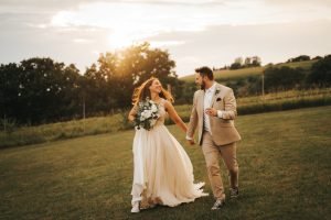 Wedding couple running towards camera in grass field