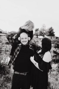 Family photo in Sioux Falls with child sitting on dad's shoulder and mom looking at her