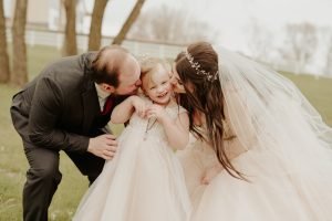 Wedding couple kissing daughter on the cheek