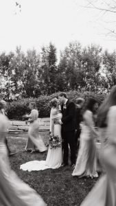 Wedding couple kissing with wedding party walking by
