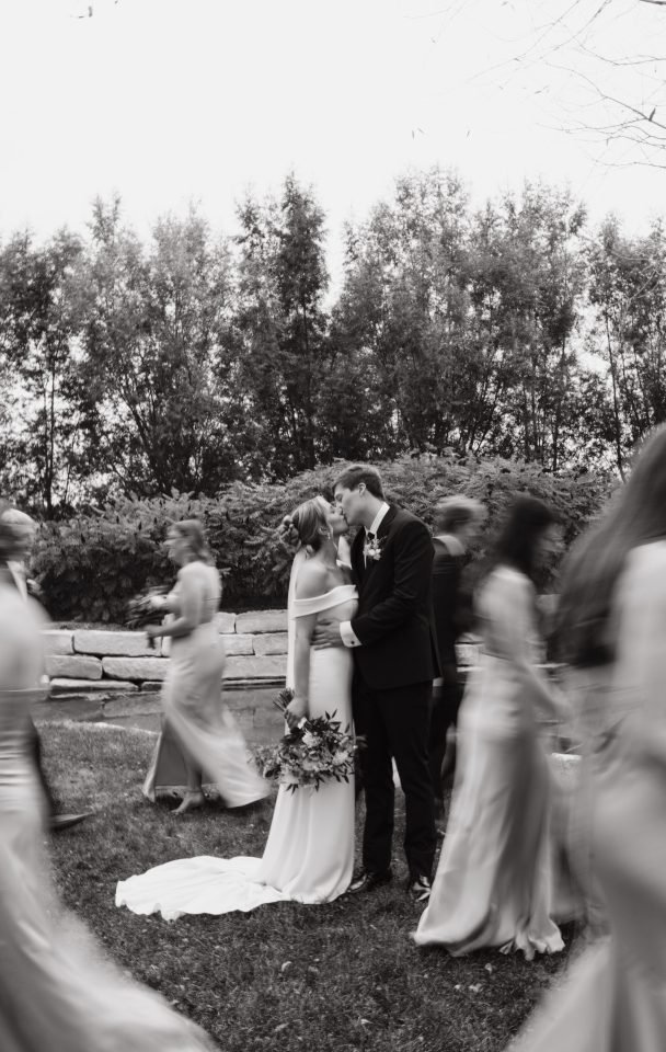 Wedding couple kissing with wedding party walking by Wedding couple kissing with wedding party walking by
