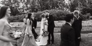 Wedding couple kissing with wedding party walking by