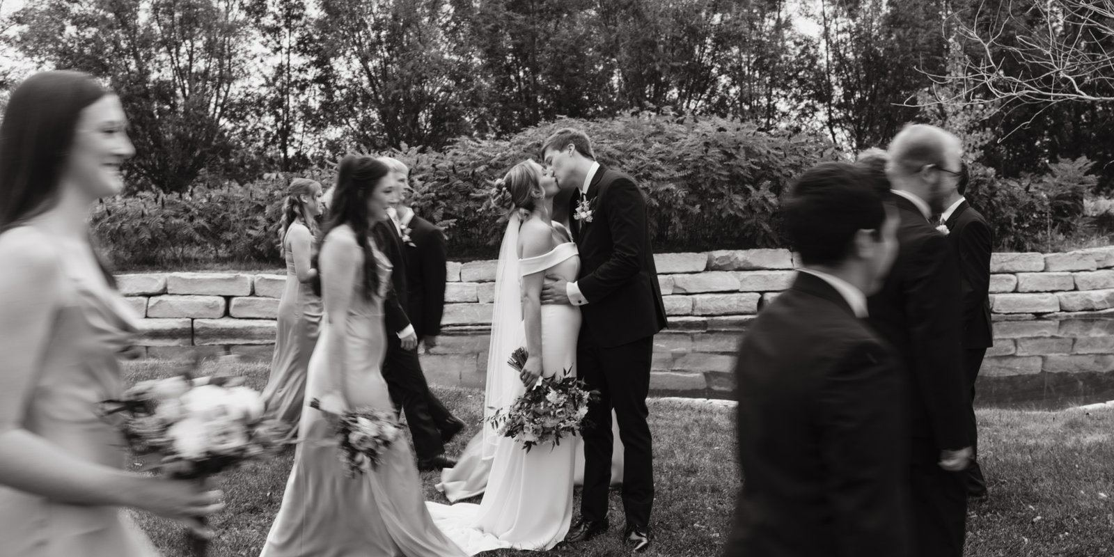 Wedding couple kissing with wedding party walking by Wedding couple kissing with wedding party walking by