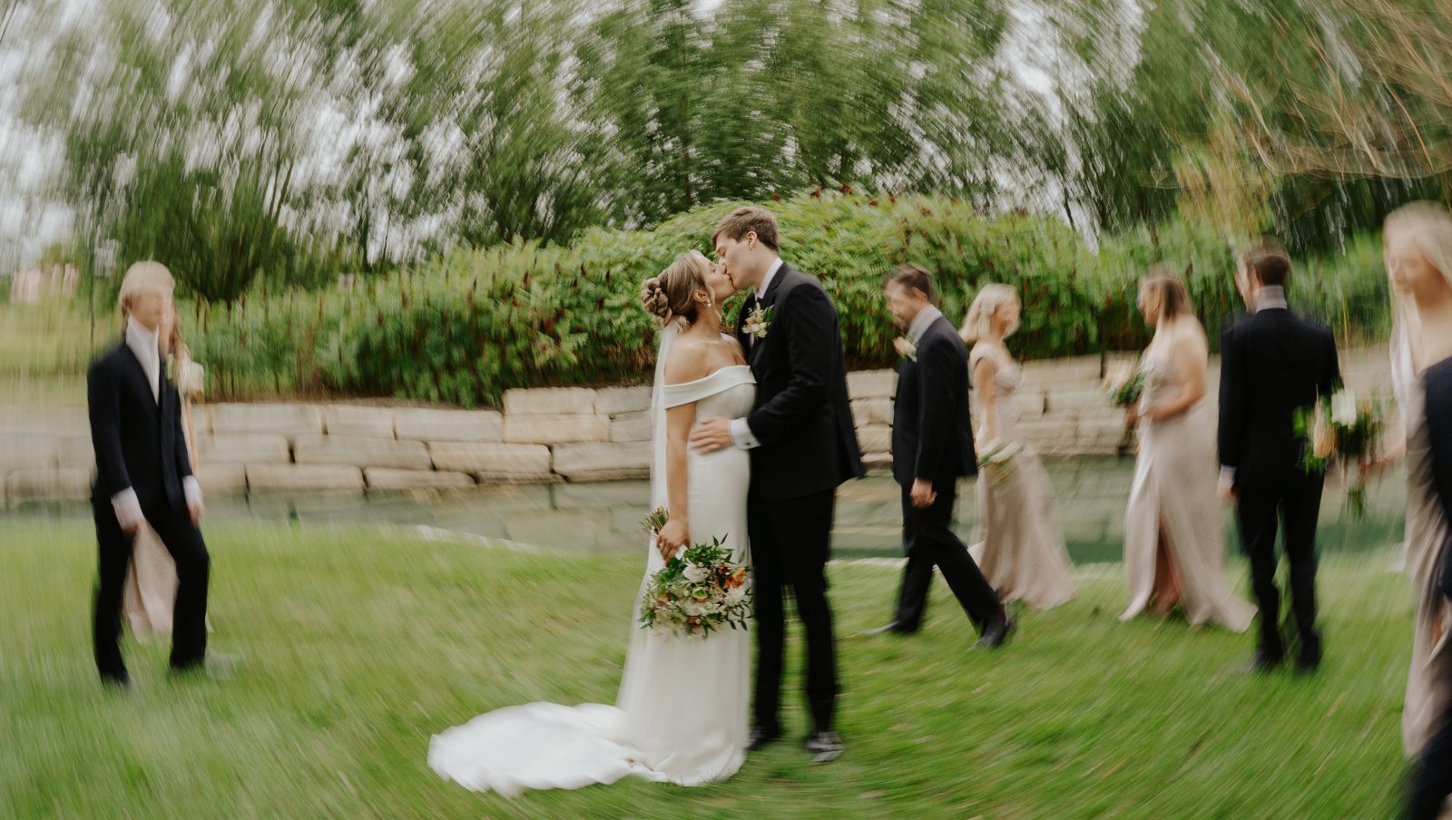 Wedding couple kissing while wedding party walks by