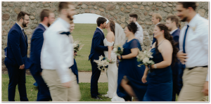 Wedding couple kissing with bridal party walking around them