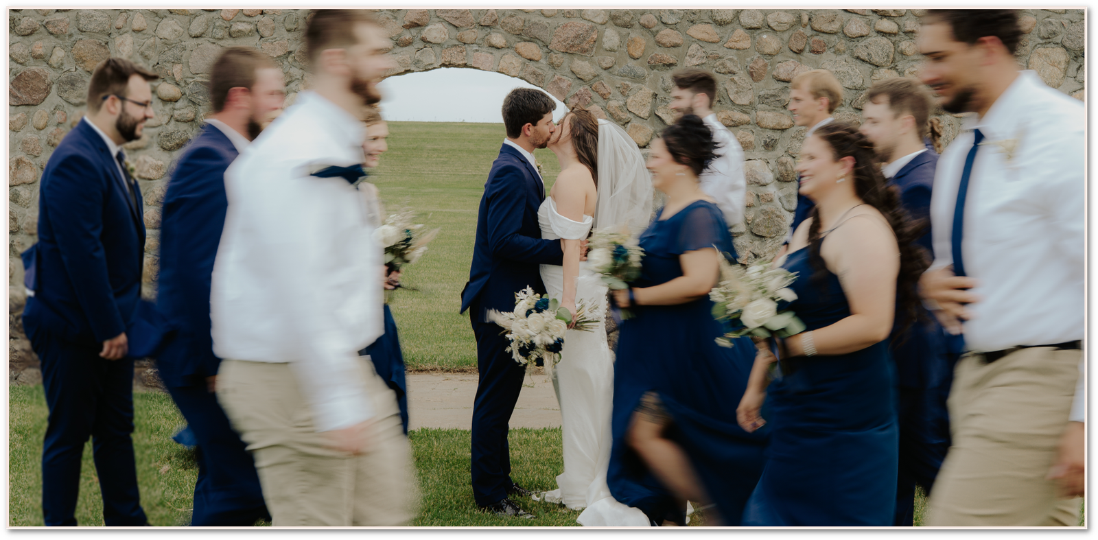 Wedding couple kissing with bridal party walking around them